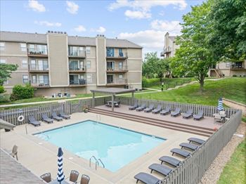 A large swimming pool surrounded by lounge chairs and apartment buildings.